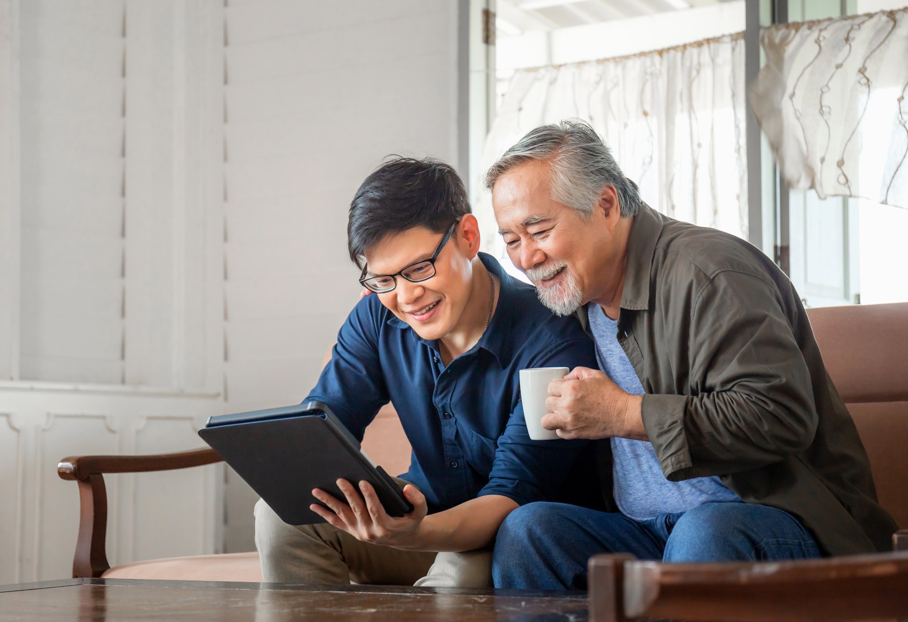 Happy Senior Asian Father and Adult Son Using Tablet Smartphone